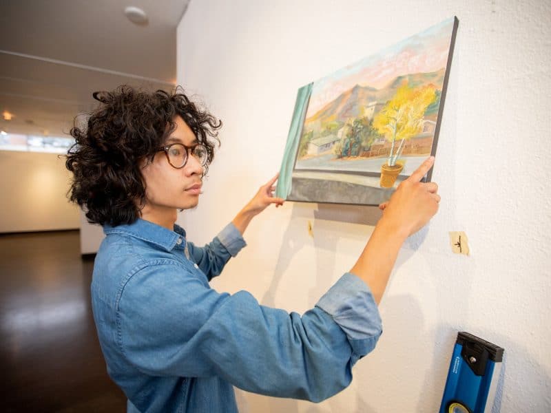 Student hangs a painting on a wall.