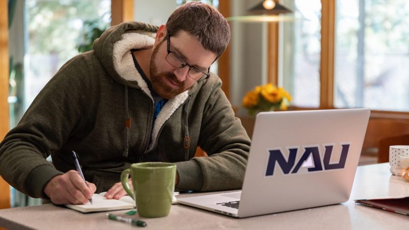 Student studies at home on laptop and writes in a notebook.