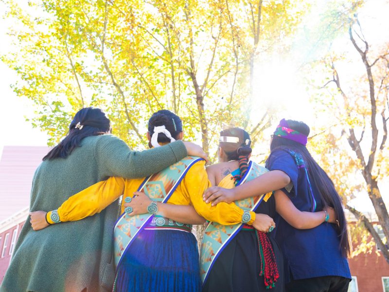 Native American students dressed in traditional garbs pose for photo.