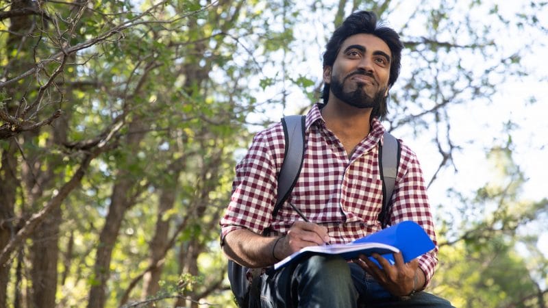 Student sits on a rock holding a notebook.