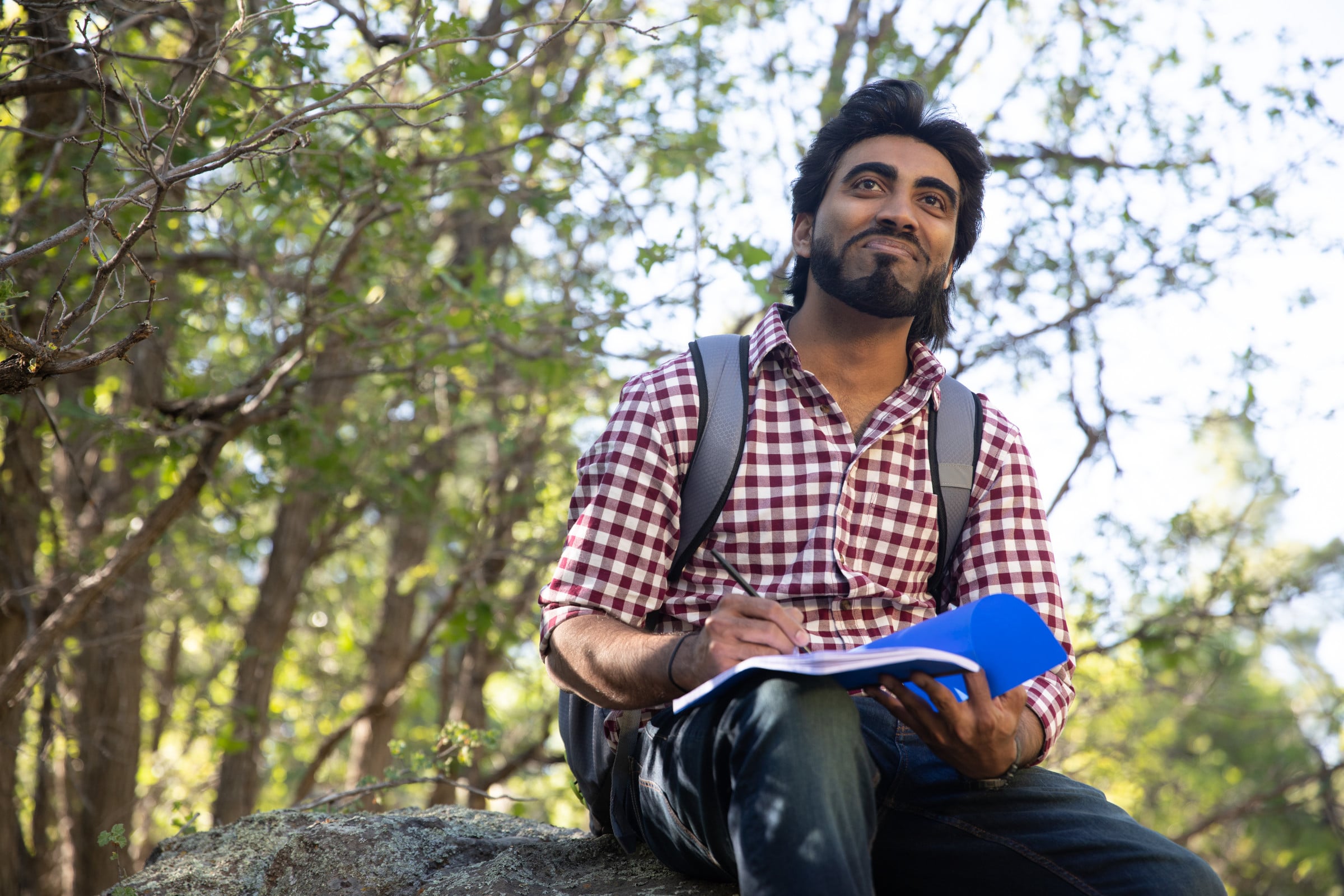 Student sits on a rock holding a notebook.