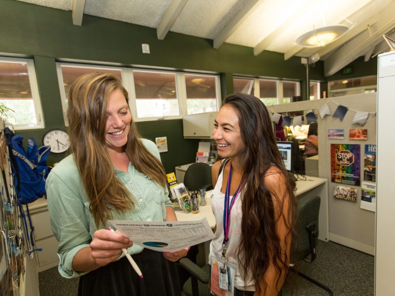 Female NAU advisor helps a smiling female student by showing her a document contain graphs and charts