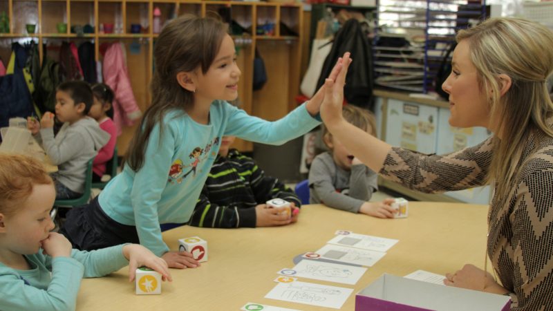 Child high fives adult in classroom.