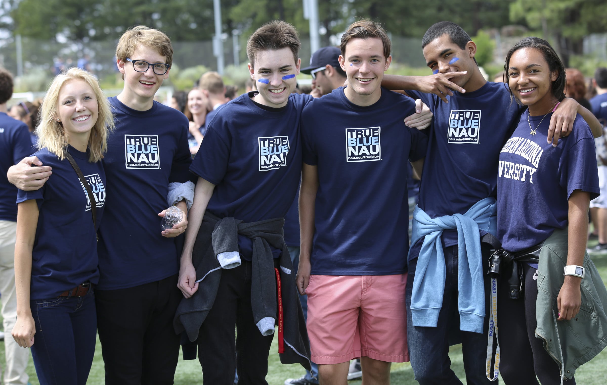 Students wearing matching shirts stand together with their arms around each other.