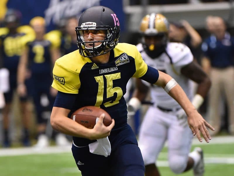 NAU football player running with football on field.