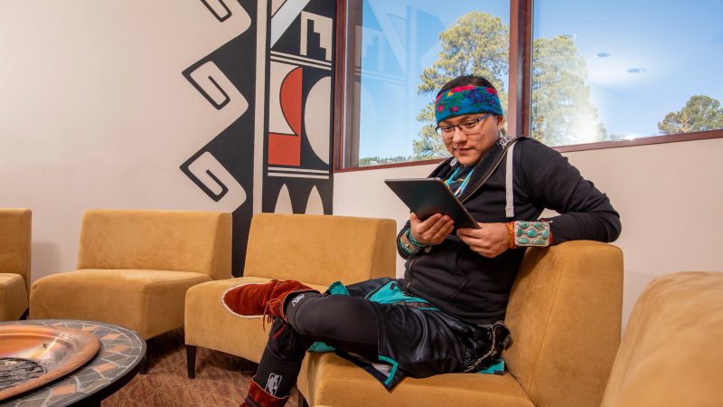 Student sits on couch and looks at tablet.