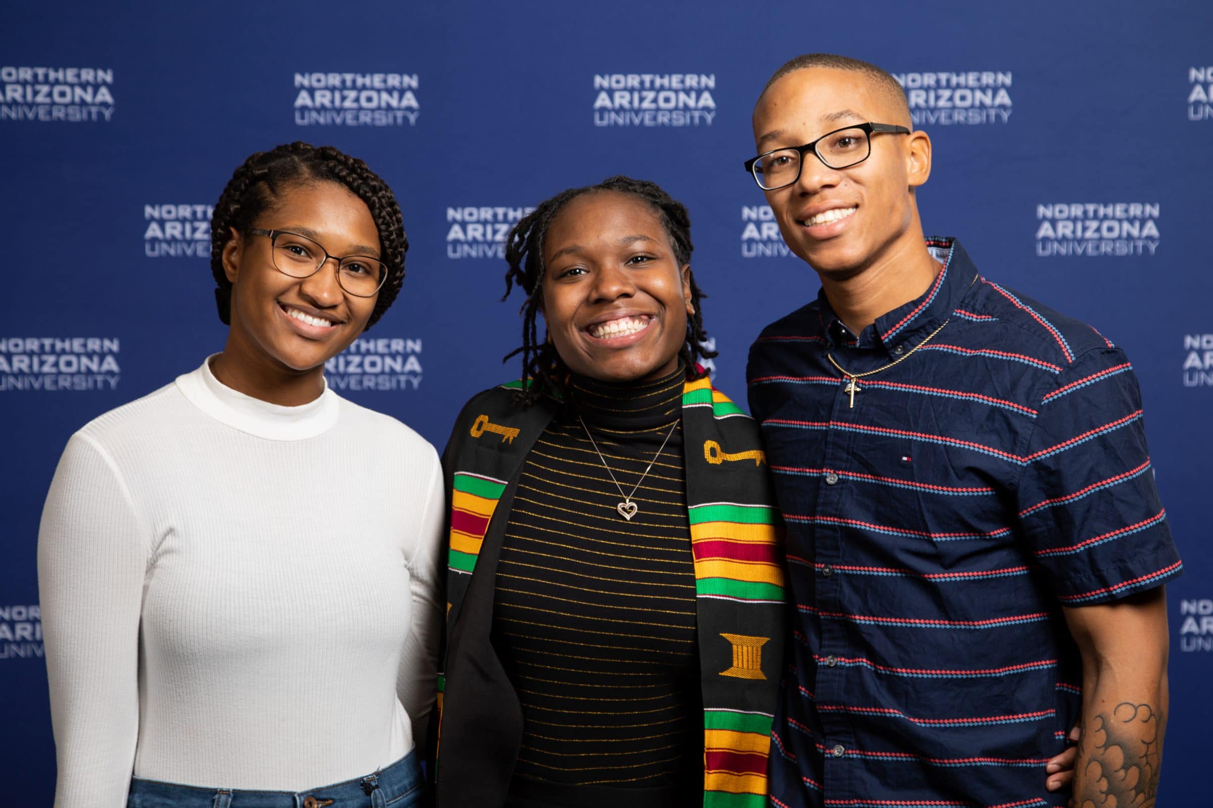 Students smile in front of NAU poster.