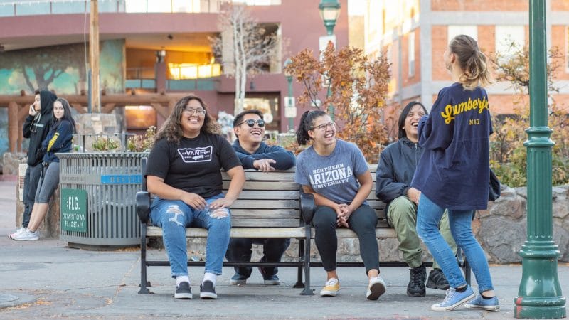 Students sit on bench, talk and laugh outside.