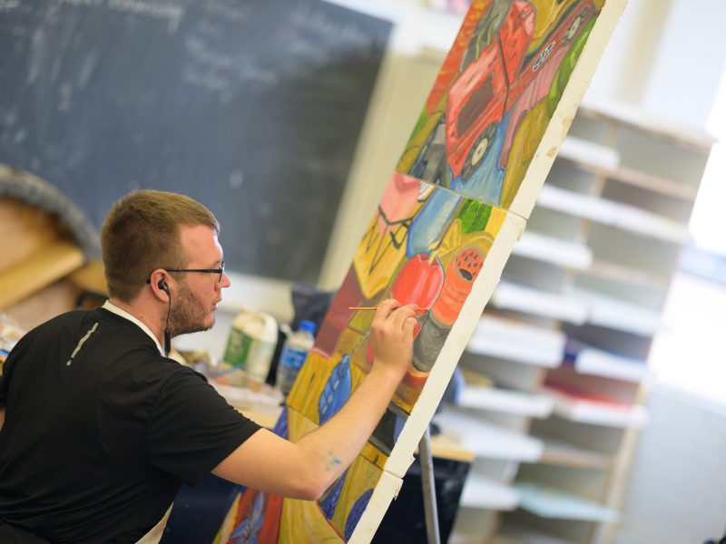 Student applies paint to canvas in art class.