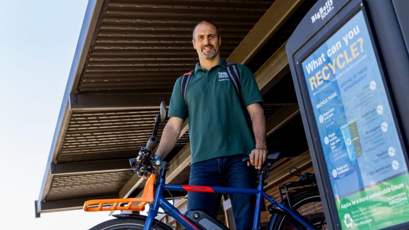 The manager of sustainability, Avi Henn stands by a recycling bin with a bike.