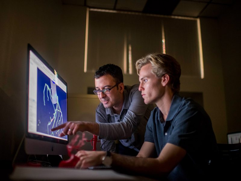 N A U director Amir Arzani studies a computer screen with a student.