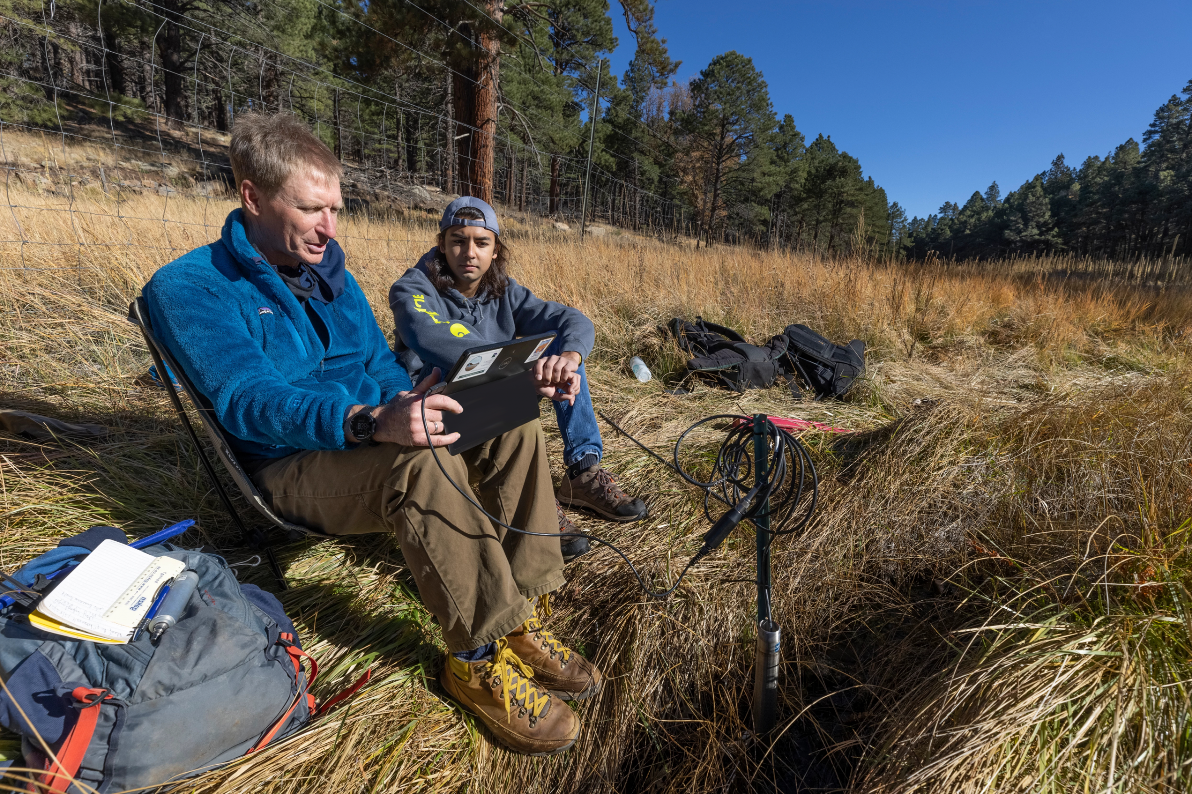 A professor and student sit outside looking at a tablet.