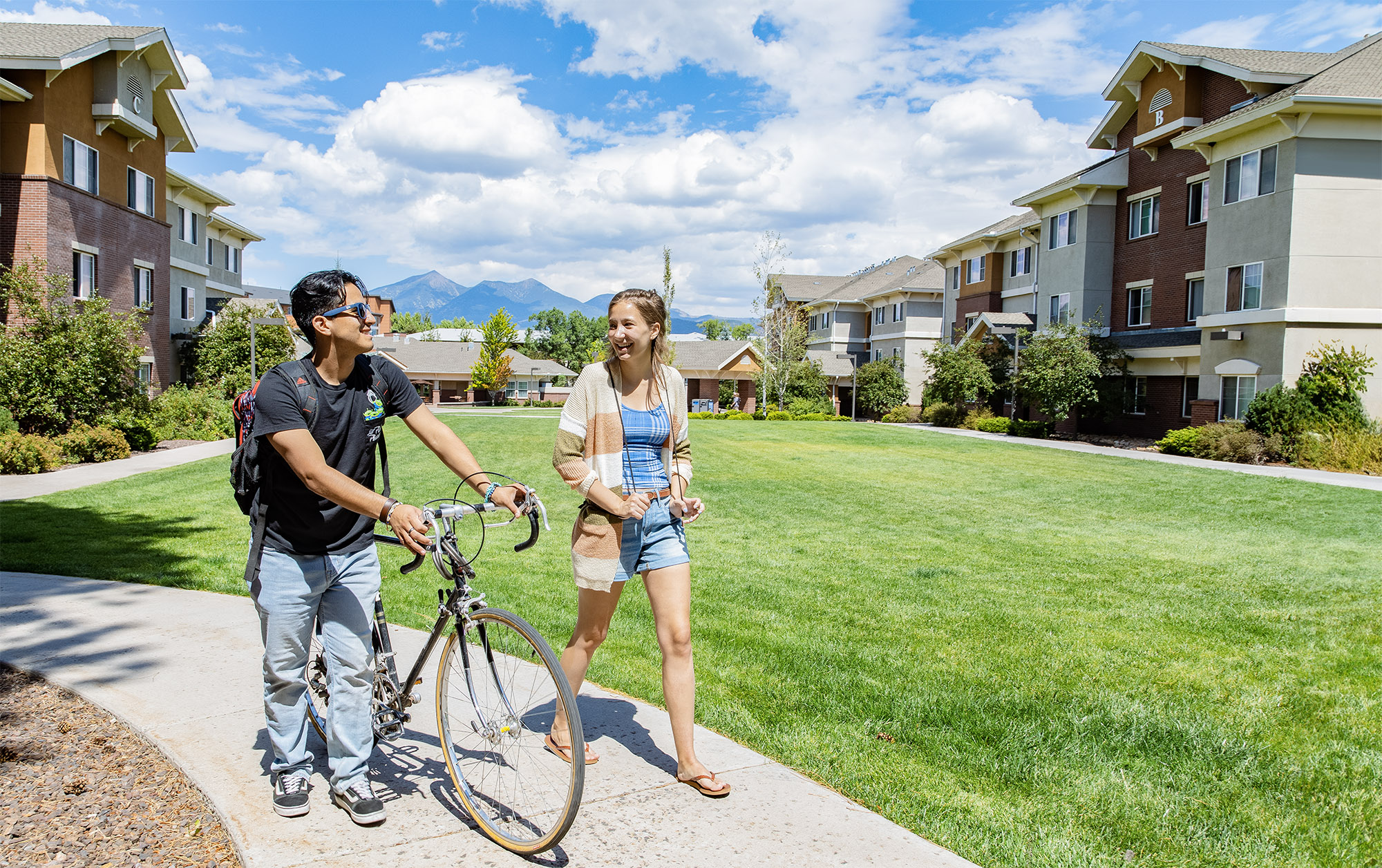 Student walks alongside cyclist on sidewalk at N A U Flagstaff campus.