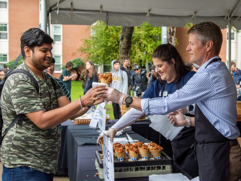 Staff serving food to a student at a barbeque.