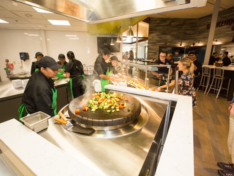 Sautéed vegetables cook on a griddle in front of hungry students at the dining hall.