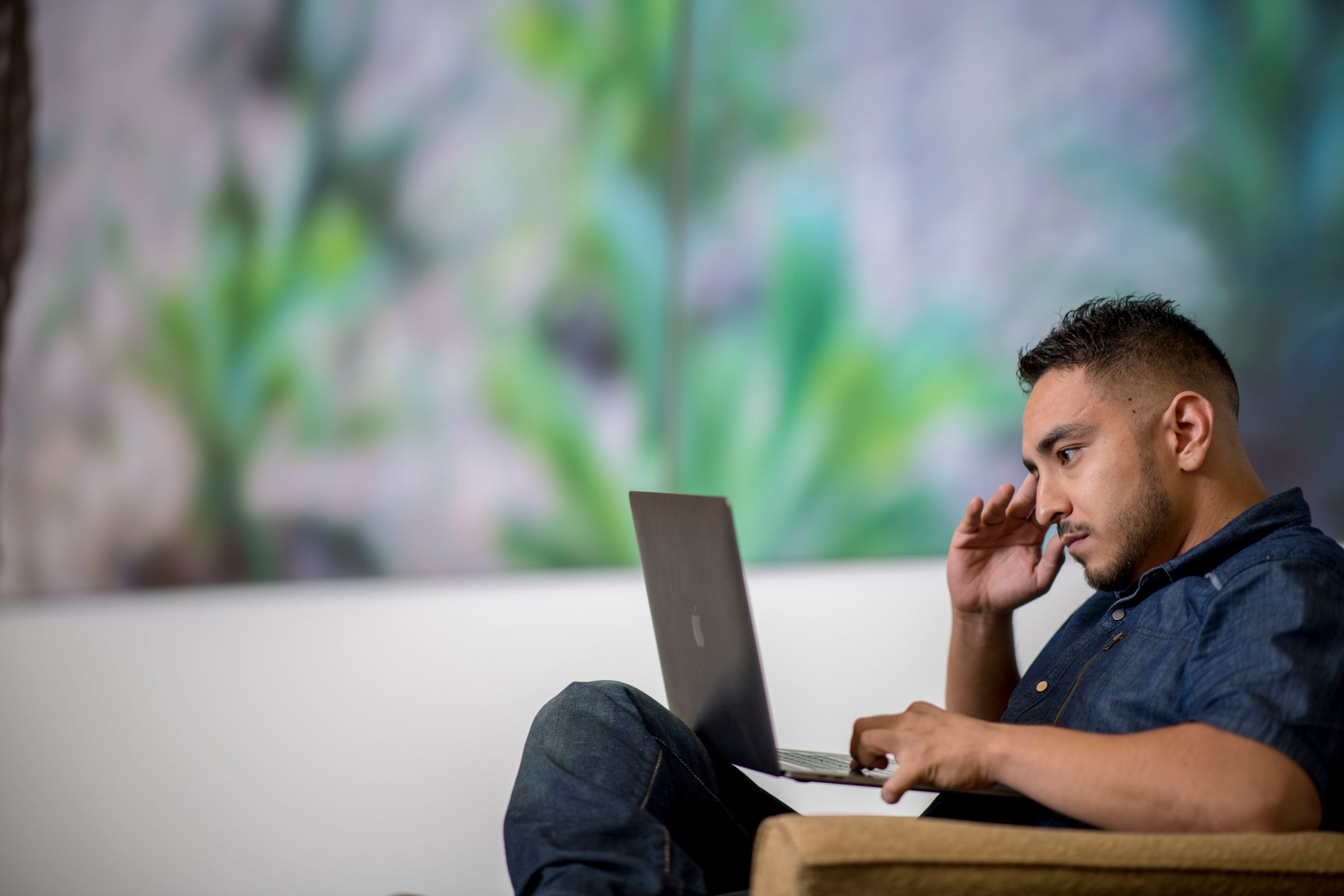 Profile view of a student sitting in a chair, looking at a laptop.
