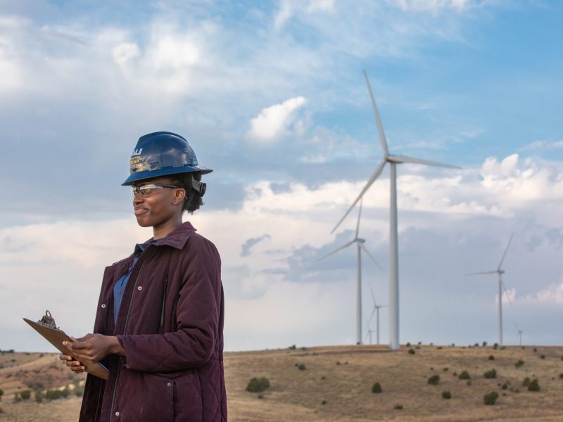 Energy student standing outside at a wind farm with a clipboard.