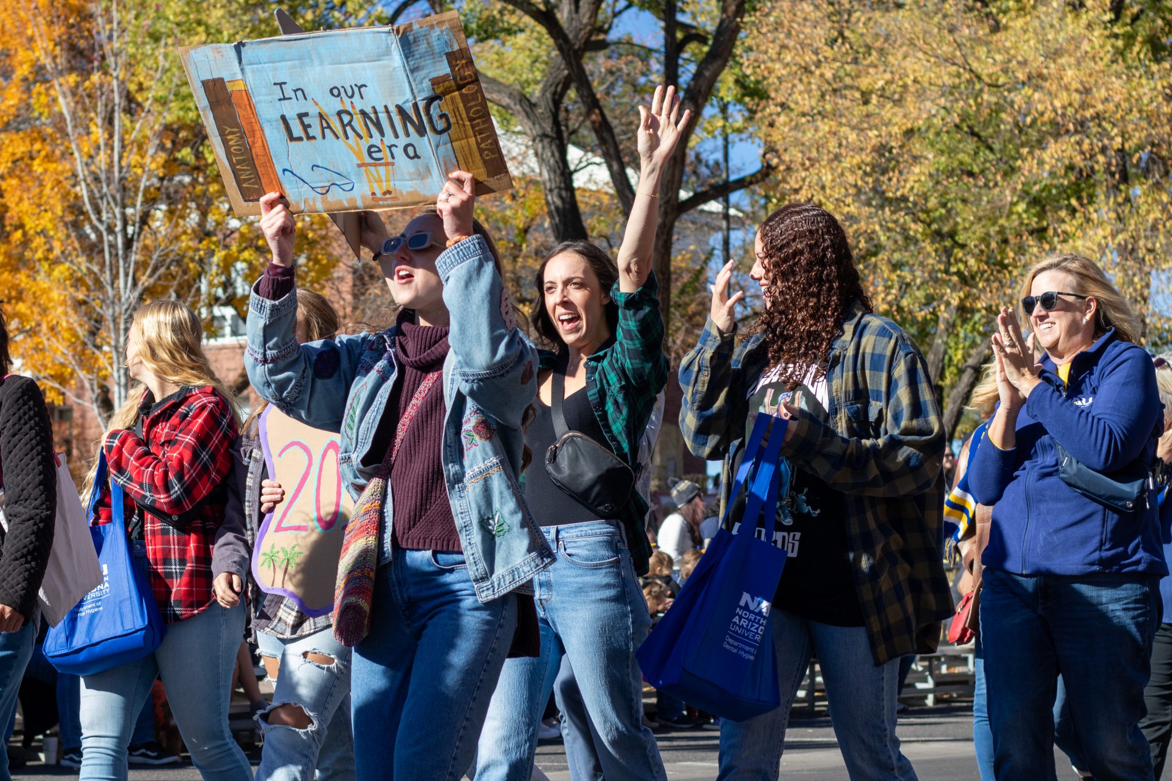 A group of people celebrating and holding hand made signs for N A U's Homecoming Parade in Flagstaff, AZ.