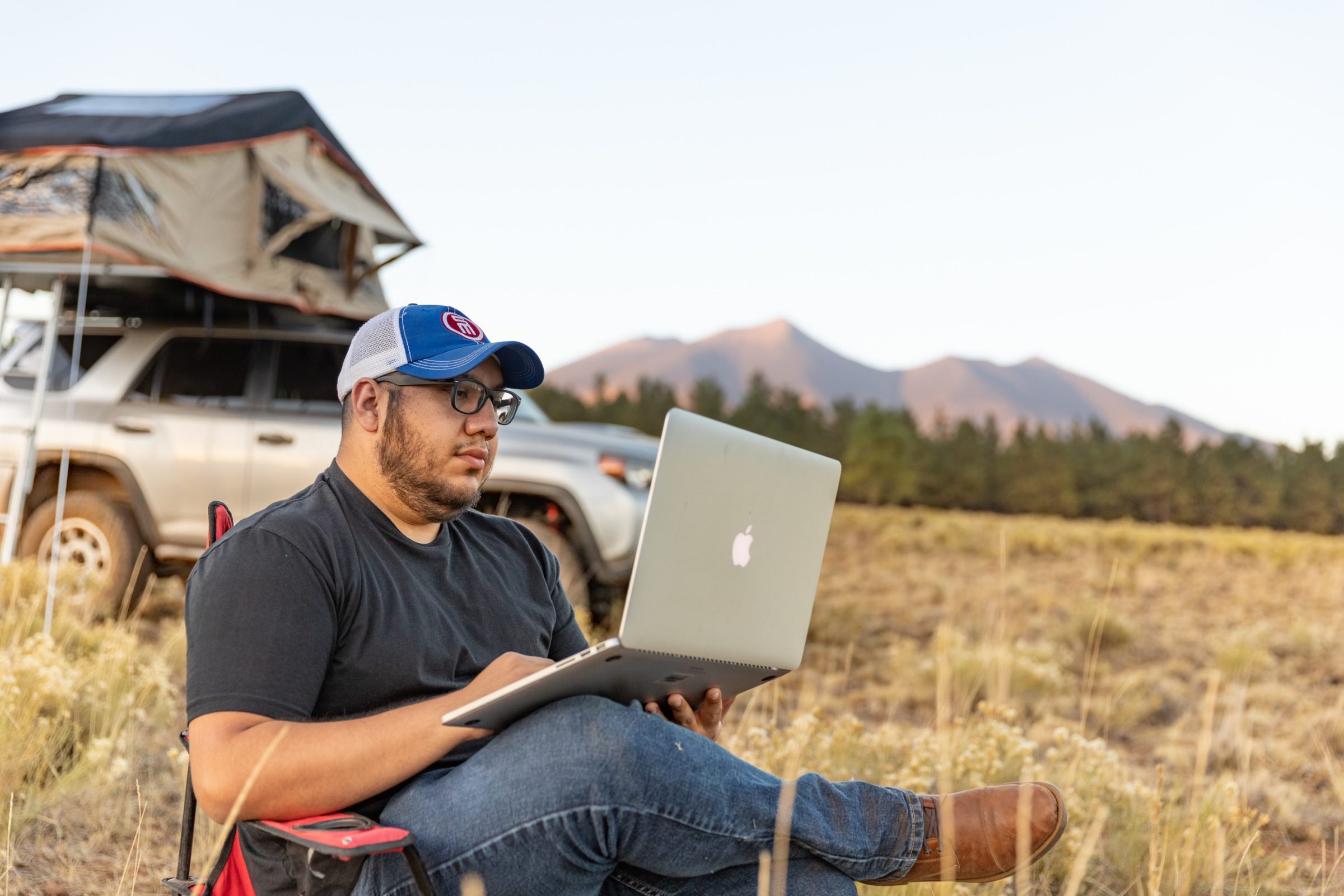 Student working on a computer while camping.