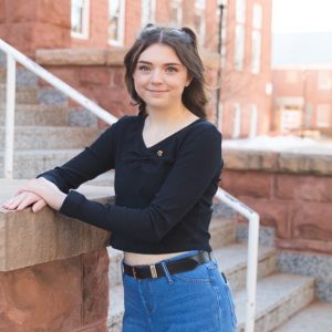 Photo of smiling Rachael Suchy in front of Old Main on NAU campus. Rachael is wearing a black long sleeve shirt with jeans.