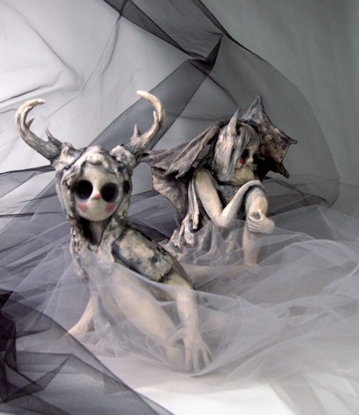 Two humanoid sculptures, one with antlers and the other with wings, posing together.