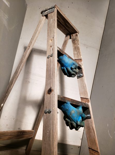 Closeup on blue hand sculptures attached to underside of ladder rungs.