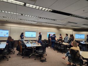Students and guests gather around digital monitors featuring posters by CCS interns in Cline Library.