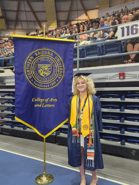 student Alex Williams stands with the blue and gold flag for the College of Arts and Letters at graduation.