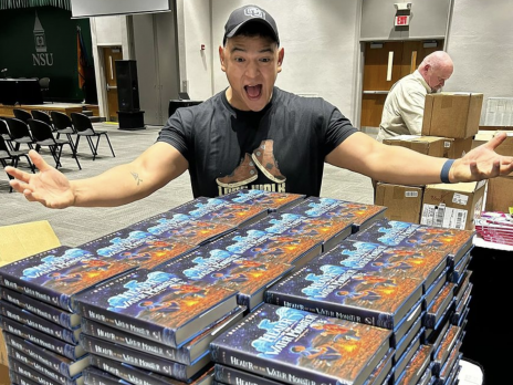 Brian Young behind stacks of his book at a speaking engagment looking very very excited