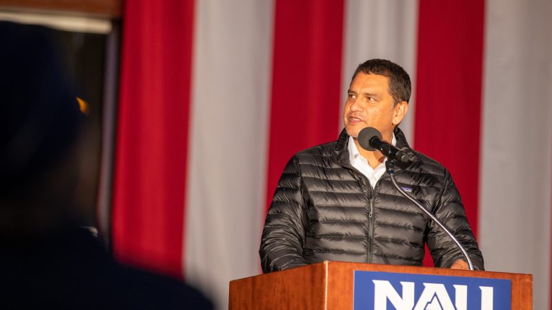 President Dr. Jose Luis Cruz Rivera speaks at a podium with an American flag in the background.