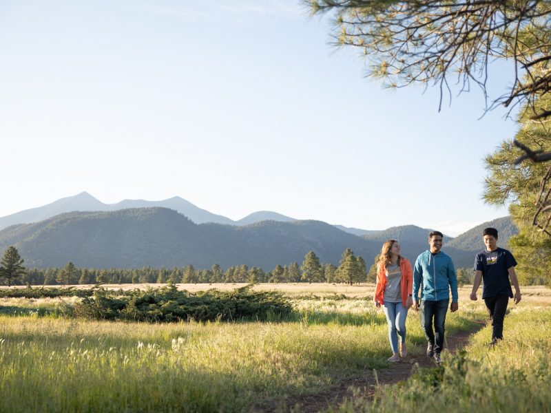 Three people on a hiking trail with mountains in the background.