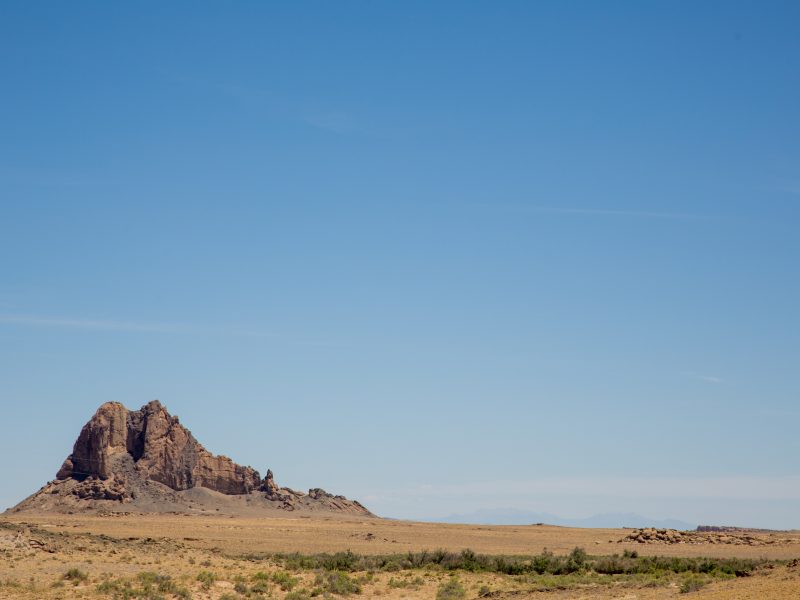Landscape photo of desert in the foreground, with a rocky bluff off to the side.