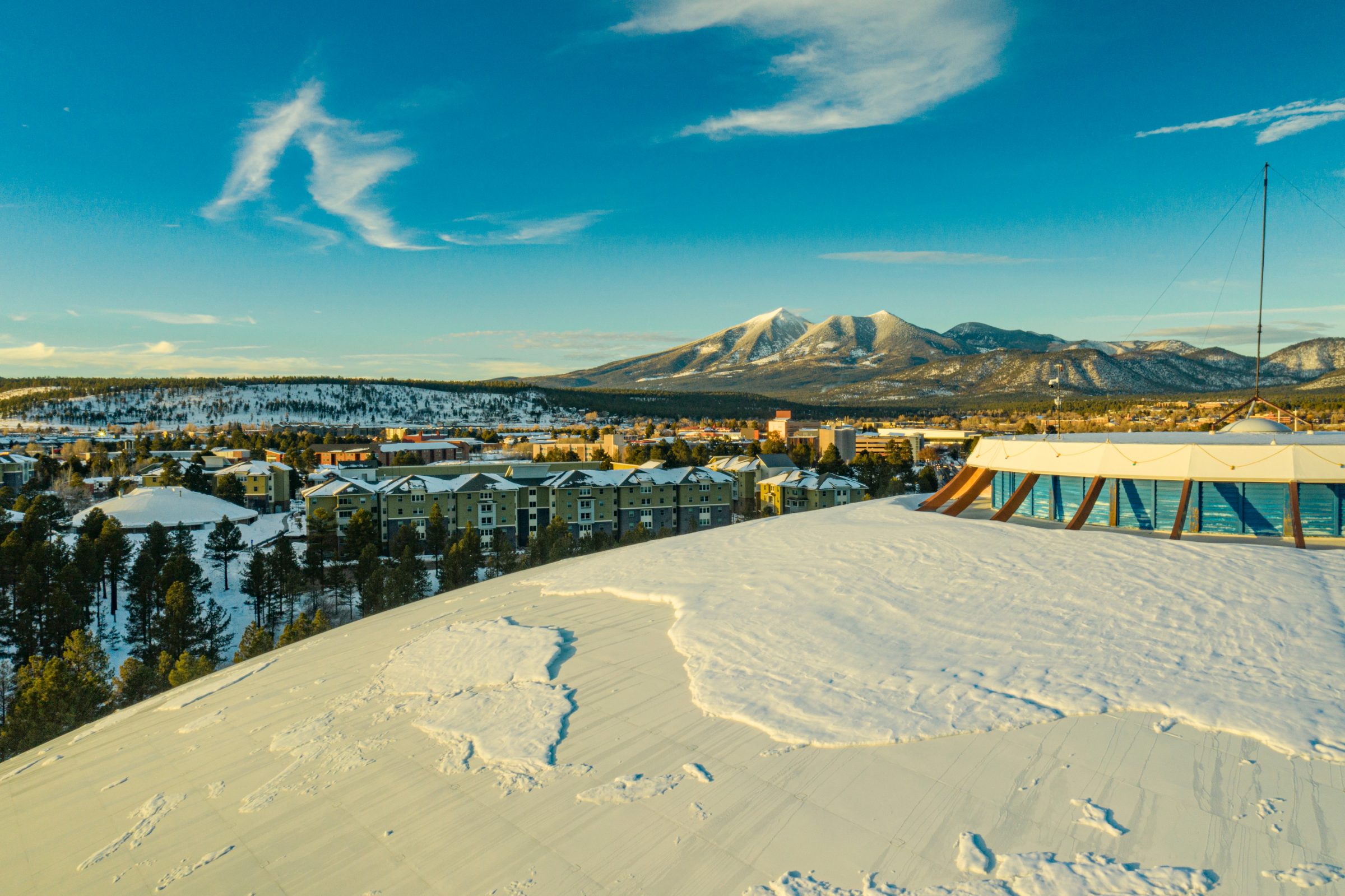 Aerial photo of N A U Flagstaff campus with snow-covered mountains in the background.