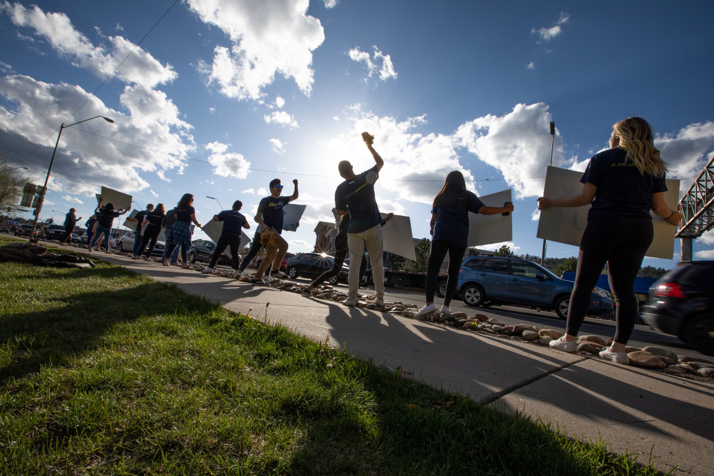 Students standing along a road holding up signs.