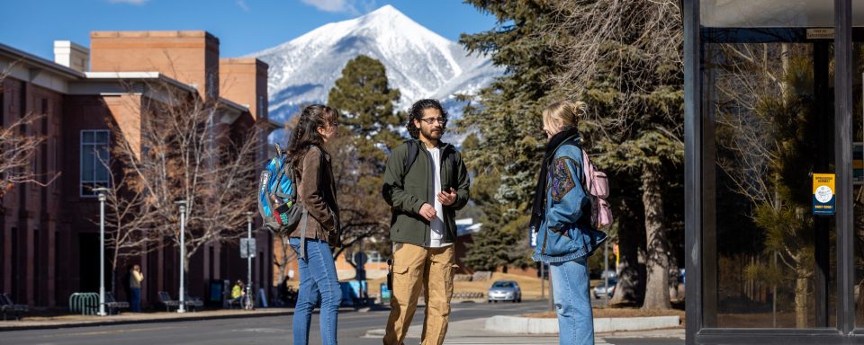 Three students talking on campus with the San Francisco Peaks in the background