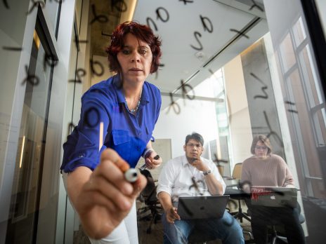 Instructor writes on glass while students watch.