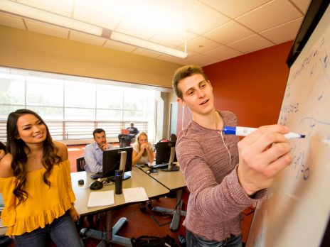 student doing a problem on a white board with three other students watching