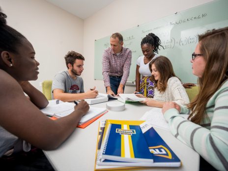 five math students being tutored by professor in a classroom