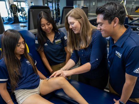 A faculty member shows three students how to perform an exam on a student's knee