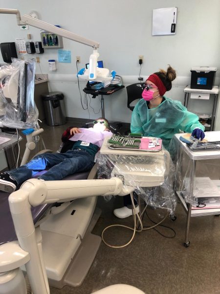 A dental hygienist cleaning a kids teeth.