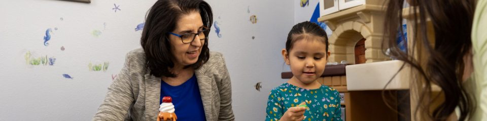 A faculty leader instructs a graduate student during a play therapy session with a young girl. 