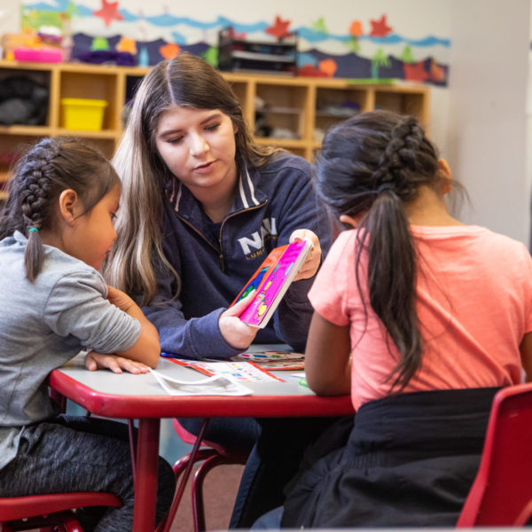 A young woman helps two elementary school students at a small table