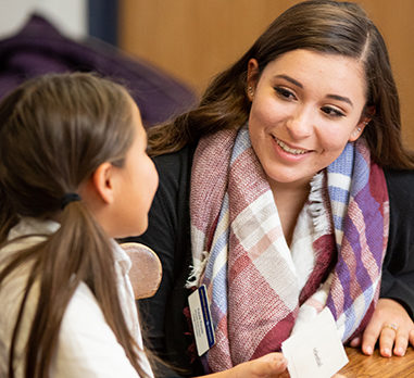 A smiling young woman speaks to a child in a classroom