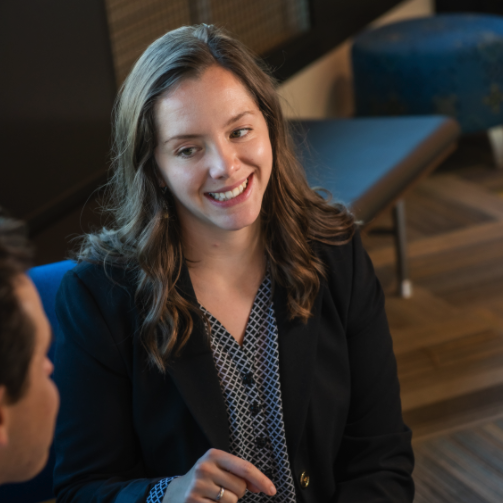 A young woman in a blazer smiles at a peer