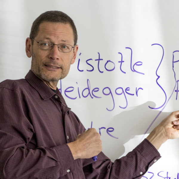 A professor writes philosophy concepts on a whiteboard