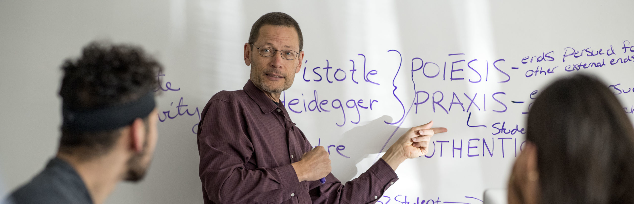 A professor writes philosophy concepts on a whiteboard