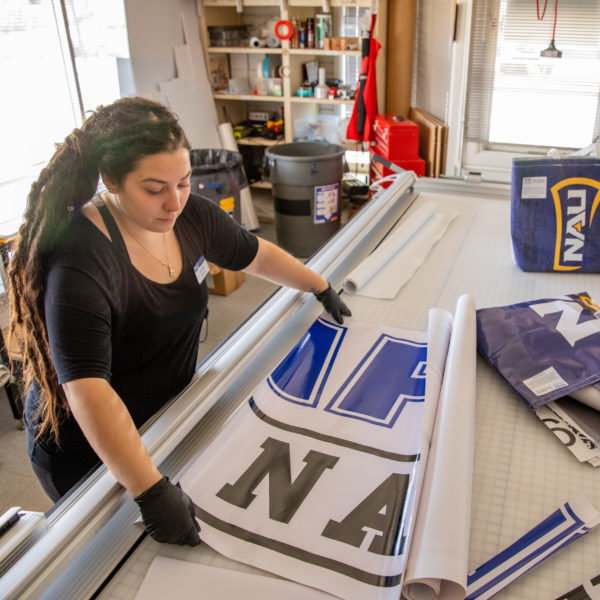 A woman measures an NAU banner on a worktable