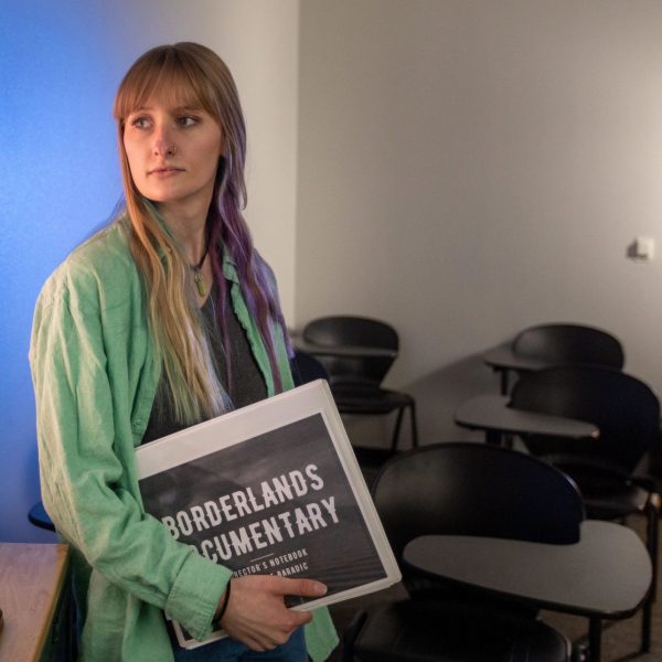 Mackenzie Baradic standing beside a large television screen while presenting her documentary film.