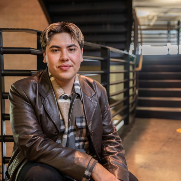 Joey Carosilva posing in the NAU School of Communication wearing a leather jacket and heavy, flannel button-down shirt.