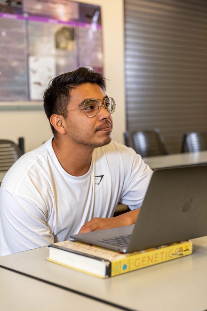 Gerardo Noriega in a classroom with a laptop and genetics textbook.